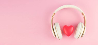 Pembe arka planda kırmızı kalp işareti olan kulaklıklar.