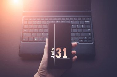 31 Temmuz. Ayın 31 'i, takvim tarihi. Laptop bilgisayarındaki el bilgisayarı, güneş ışığı alan karanlık bir arka plan. Yaz ayı, yılın günü konsepti.