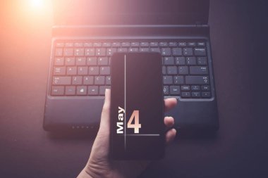 4 Mayıs. Ayın dördüncü günü, takvim tarihi. Laptop bilgisayarındaki el bilgisayarı, güneş ışığı alan karanlık bir arka plan. Bahar ayı, yılın günü konsepti.