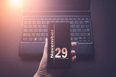 29 Kasım. Ayın 29 'u, takvim tarihi. Laptop bilgisayarındaki el bilgisayarı, güneş ışığı alan karanlık bir arka plan. Sonbahar ayı, yılın günü konsepti.