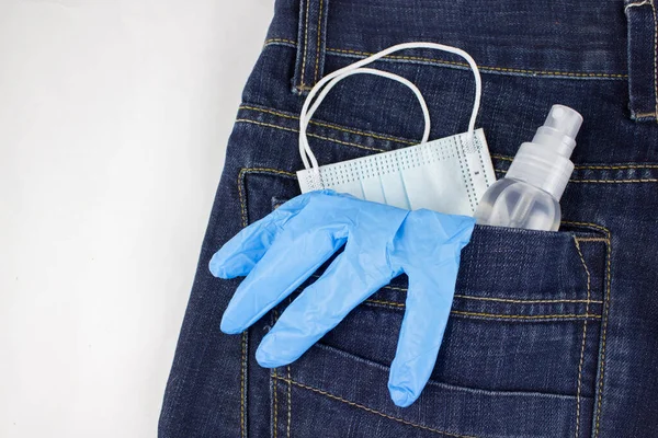 Blue medical mask, gloves and hand sanitizer spray looks out from back jeans pocket, close up. Healthcare concept