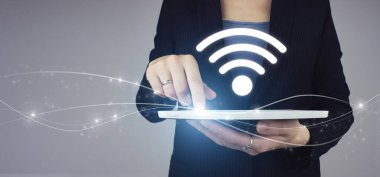 Ücretsiz WiFi ağ sinyali teknolojisi internet kavramı. Beyaz tablet iş kadınının elinde, gri arkaplanda dijital hologram Wi-Fi işareti var. İş ağı bağlantı kavramı.