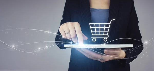 Beyaz tablet iş kadını elinde dijital hologram alışveriş arabası simgesi ile gri arka planda. Çevrimiçi Dijital Pazarlama