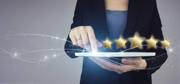 Increase rating or ranking, evaluation and classification idea. White tablet in businesswoman hand with digital hologram Five stars 5 rating sign on grey background. Review, Rating,Satisfaction.