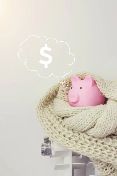Pink piggy bank on radiator with digital hologram dollar in cloud thought above his head on blue background. Concept of paying for heating in home.