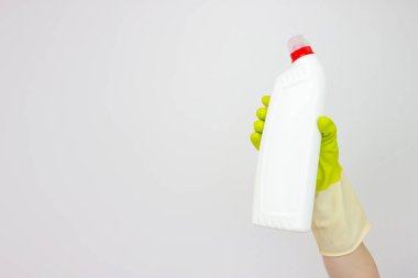 Spring cleaning concept. Top view of hand in yellow rubber gloves holding bottle of detergent on grey background. Cleaning supplies concept