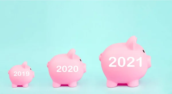 Pink piggy bank in the shape of pig with digital hologram 2021 year sign on blue background. Money saving for future investment and retirement concept