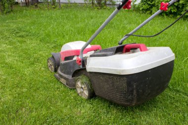 Lawn mower cutting green grass in backyard. Lawn mower on fresh green lawn.