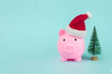 Mavi arka planda noel ağacı olan Noel Baba şapkalı domuz kumbarası. Yeni yılın sembolü
