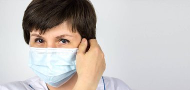 Koronavirüsü bitir. Kapatma sona erdi. Tıp doktoru maskeyi yüzünden çıkardı. Kadın bir doktor mavi arka planda koruyucu bir maskeyi çıkartıyor. Virüsle savaş. Hastalıktan kurtulma