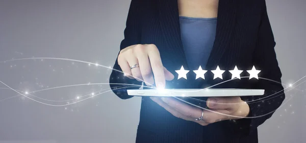 Müşteri Tecrübesi Konsepti, En İyi Mükemmel Hizmetler. Beyaz tablet iş kadını elinde dijital hologramla Gri üzerine 5 yıldızlı işaret. Yükselen beş yıldızın dokunuşu