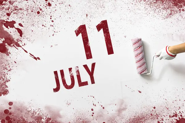 July 11st . Day 11 of month, Calendar date. The hand holds a roller with red paint and writes a calendar date on a white background. Summer month, day of the year concept
