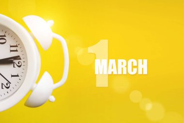 1 Mart. Ayın ilk günü, takvim tarihi. Takvim günüyle birlikte sarı arka planda beyaz çalar saat. Bahar ayı, yılın günü konsepti.