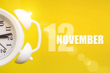 12 Kasım. Ayın 12 'si, takvim tarihi. Takvim günüyle birlikte sarı arka planda beyaz çalar saat. Sonbahar ayı, yılın günü konsepti.