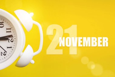 21 Kasım. Ayın 21 'i, takvim tarihi. Takvim günüyle birlikte sarı arka planda beyaz çalar saat. Sonbahar ayı, yılın günü konsepti.
