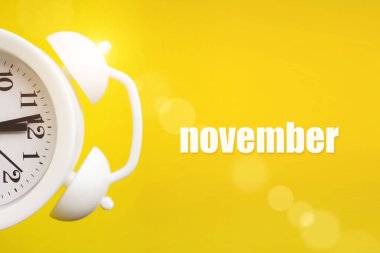 Kasım. Ay, takvim ayı. Takvim günüyle birlikte sarı zemin üzerinde beyaz alarm saati. Sonbahar, yılın ayı konsepti.