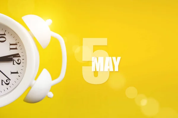 May 5th. Day 5 of month, Calendar date. White alarm clock on yellow background with calendar day. Spring month, day of the year concept