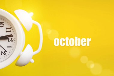 Ekim. Ay, takvim ayı. Takvim günüyle birlikte sarı zemin üzerinde beyaz alarm saati. Sonbahar, yılın ayı konsepti.