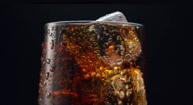 Glass of cola with ice cubes on black background, close-up