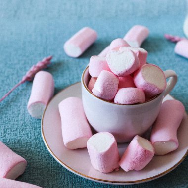 Mavi arka planda tatlı pembe şekerlemeler. Bir marşmelov bir kalp şeklindedir. Kurumuş pembe çiçeklerle birlikte. Kadın imajı, tapılası ve Instagram hikayeleri için ideal bir şekli var.
