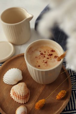 Deniz kabuklarının yanında bir fincan kahve, lacivert bir bez ve beyaz kurumuş çiçekler. Deniz konsepti. Tatil hazırlığı. Tatil hatırası..