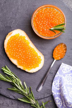 Siyah arka planda kırmızı somon havyarlı sandviç ve biberiye..