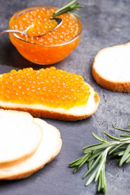 Siyah arka planda kırmızı somon havyarlı sandviç ve biberiye..