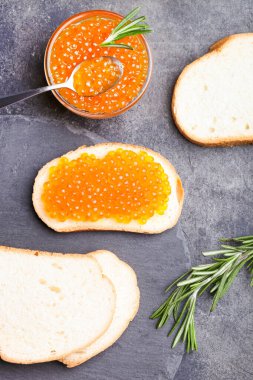 Siyah arka planda kırmızı somon havyarlı sandviç ve biberiye..