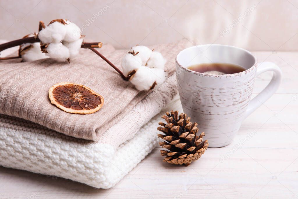 Warm winter sweaters and a cup of hot tea on a white wooden background.