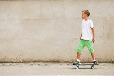 Çocuk duvarın arka planında kaykay sürüyor. Aktif spor.