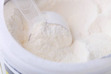 Kavanozdaki beyaz protein tozunun ölçüm kaşığıyla yakın çekimi.