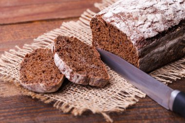 Bir somun dikdörtgen çavdar ekmeği ahşap kahverengi arka planda çuval bezi üzerinde.