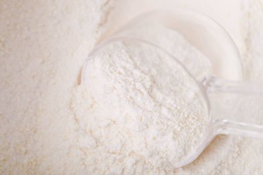 Kavanozdaki beyaz protein tozunun ölçüm kaşığıyla yakın çekimi.