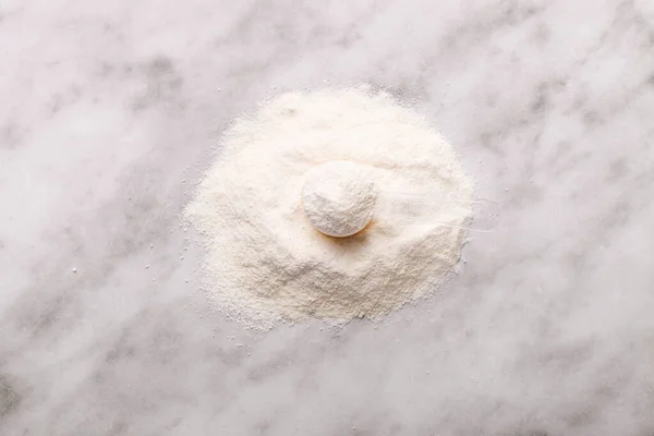 Heap of white protein powder with measuring spoon on marble background.