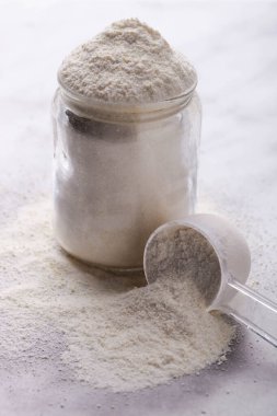 Kavanozda beyaz protein tozu ve mermer arka planda ölçüm kaşığı..