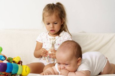 Küçük tatlı çocuk yeni doğan kardeşini öpüyor. Küçük çocuk yeni doğan kardeşiyle tanışıyor. Beyaz bir fedaide battaniyenin altında uyuyan bir bebek. Çocuklar oynuyor ve kaynaşıyorlar. Küçük yaş farkı olan çocuklar.