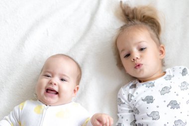 Küçük tatlı çocuk yeni doğan kardeşini öpüyor. Küçük çocuk yeni doğan kardeşiyle tanışıyor. Beyaz bir fedaide battaniyenin altında uyuyan bir bebek. Çocuklar oynuyor ve kaynaşıyorlar. Küçük yaş farkı olan çocuklar.