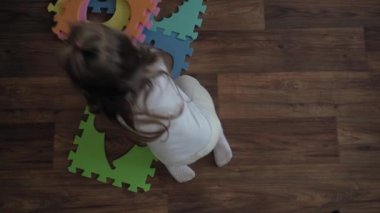 Çocukluk, aile, izolasyon kavramı. Küçük bir anaokulu çocuğu kahverengi zeminde oturan büyük parçaların yumuşak bulmacalarını topluyor. Çocuklar. Erkek ve kız kardeş evde motor becerileri için eğitim oyunları oynuyor.