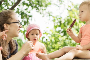 Hafifçe odaklan. Tatil, çocukluk, annelik, yemek kavramı. Annem kardeşlerinin dondurmasına bakıyor. 2-3 yaşlarındaki çocuklar bahçede buzlu şeker yiyorlar. Mutlu çocuklar piknikte tatlıdır.
