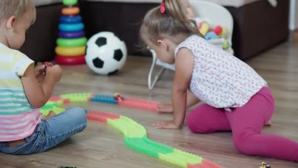 Infância, jogos, educação e conceito de desenvolvimento - plano geral de crianças pequenas menino irmão e menina irmã bebê brincar com estrada mágica na sala de jogos infantil. Os irmãos se divertem em casa em quarentena — Vídeo de Stock