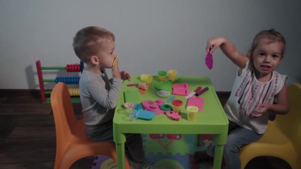 Medizin, Familie, Spiel, Kindheit, Kunstkonzepte - zwei glückliche kleine Kinder spielen während der Quarantäne mit farbigem Knetgummi am heimischen Tisch. Geschwister haben Spaß beim gemeinsamen Lernen — Stockvideo