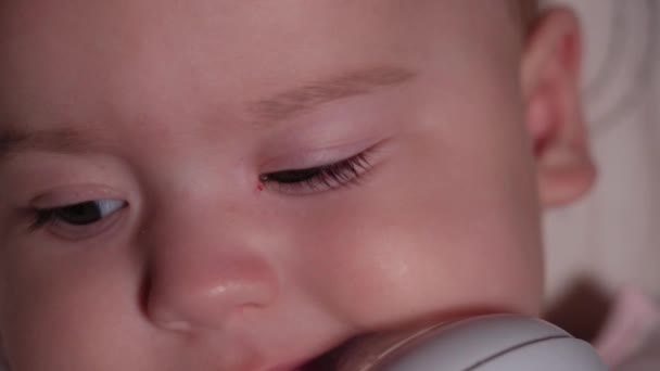 Criança, infância, conceito de emoção - Extremo close-up de rosto sorridente de recém-nascido de olhos castanhos bebê desdentado acordado 7 meses de idade beber água de garrafa com mamilo deitado em macacão branco no carrinho — Vídeo de Stock