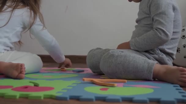 Kindheit, Familie, Isolationskonzept - Gruppe zwei kleine Kinder sammeln weiche Puzzleteile, die auf dem Boden sitzen. Kinder Bruder und Schwester spielen Lernspiele für die Motorik zu Hause — Stockvideo