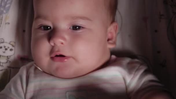 Kojenec, dětství, emoční koncept - detailní záběr roztomilé usměvavé tváře hnědookého baculatého novorozence probuzeného bezzubé miminko 7 měsíců staré dívající se na kameru ležící v bílém obleku s velkým teether v kočárku — Stock video