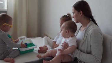 Tıp, aile, oyun konseptleri konsantre, oyuncu çocuklar tıbbi gözlük takıyor, stetoskop kullanıyor. Doktor gibi davran, hemşire gibi, dinle gülümse anne. Yeni doğmuş bebek kız kardeşim derin nefes al, yatağa otur.