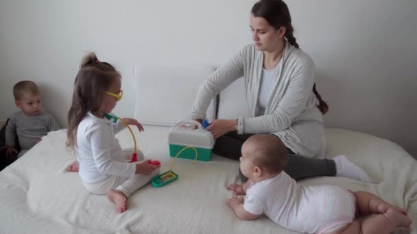 Medizin, Familie, Spielkonzepte - konzentrierte spielerische kleine Kinder tragen medizinische Brillen mit Stethoskop. Vorgeben, Arzt, Krankenschwester, hören Lächeln mommy.newborn Baby Schwester tief atmen, sitzen auf dem Bett — Stockvideo