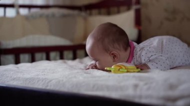 çocukluk, çocukluk, ebeveynlik, gelişim, tıp ve sağlık konsepti - ön plan, yakın plan, bebek yüzlü, tombul, yeni doğmuş bebek, yumuşak pembe tulumuyla neşeli uyanıklık, yatak odasında arkada diş çıkarma oyuncağıyla gülümsüyor.
