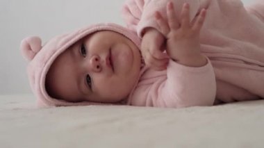 Bebek, çocukluk konsepti, gülümseyen mutlu tombul, kahverengi gözlü, yeni doğmuş çocuğun tombul yüzünün yakın çekimi. Dişsiz, 7 aylık bebek buruşuklukları, gözlerini kapatır pembe yatakta yatar evde bağcıkla.