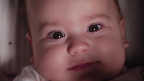 Дитяча, дитинча, емоційна концепція - екстремальне крупним планом усміхнене обличчя пухнастоокого новонародженого немовляти, якому 7 місяців, дивлячись на камеру, що лежить у білому костюмі в колясці. М'який фокус — стокове відео