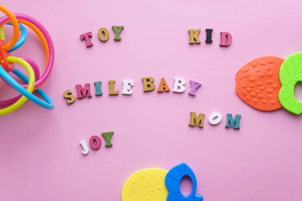 Infancia, cuidado, higiene, bebés - La palabra dientes de bebé, juguete, sonrisa, mamá, alegría dispuestos de letras de madera de colores sobre un fondo de color rosa pastel. juguete de palillo de colores grandes. kisd personal dentición copia —  Fotos de Stock